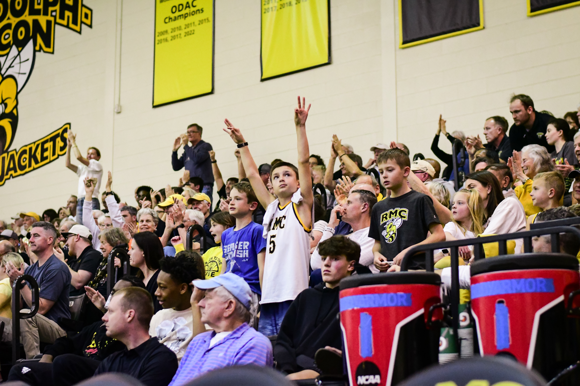 Young Randolph–Macon fans cheering in the stands beneath the Yellow Jackets banners